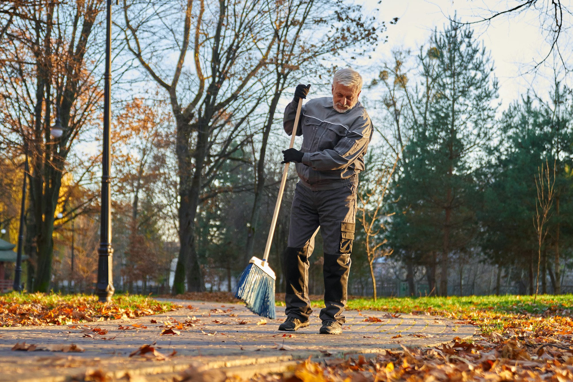 Maintenance worker cleaning roads with plastic garden broom.